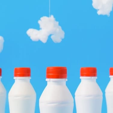 3 white milkbottles with red caps against a sky blue background with white clouds