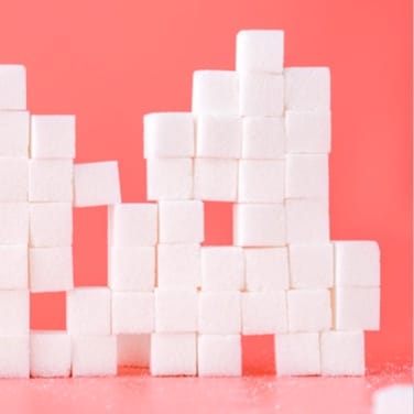 Numerous white sugar cubes stacked on top of a pink table in front of a slightly darker pink wall.